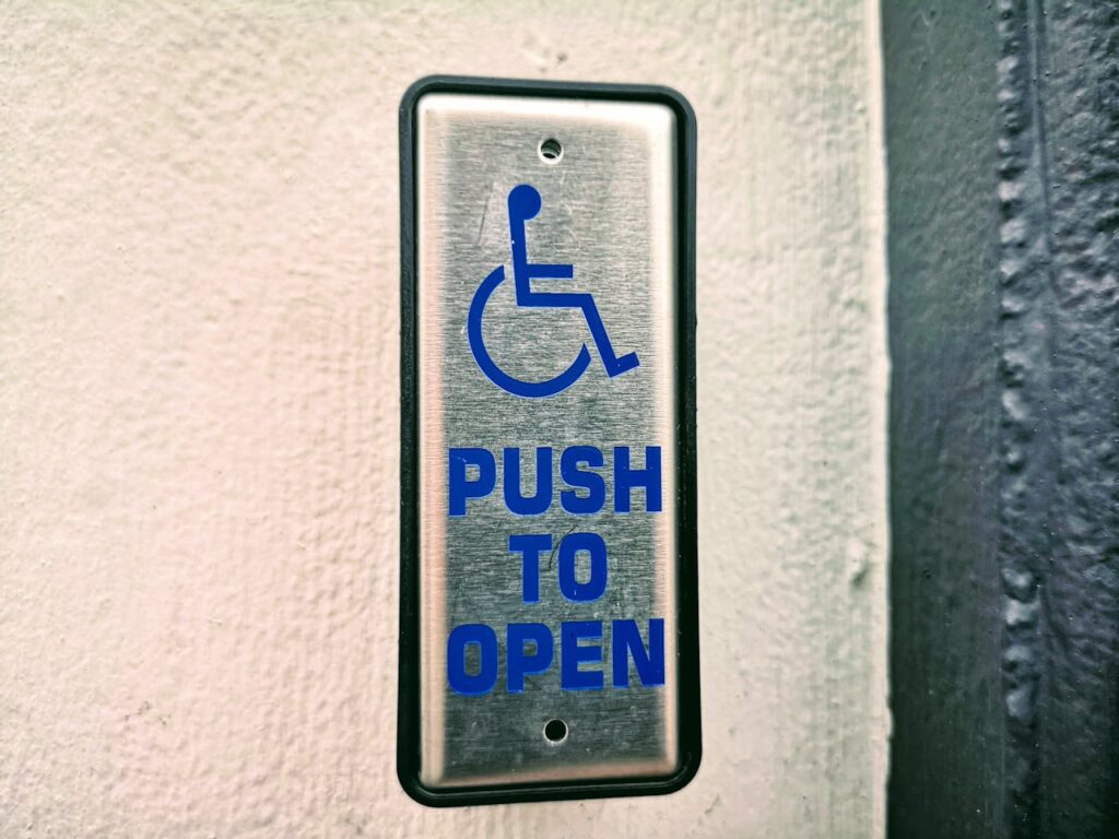 Close-up of a push button sign for accessibility on a white wall.