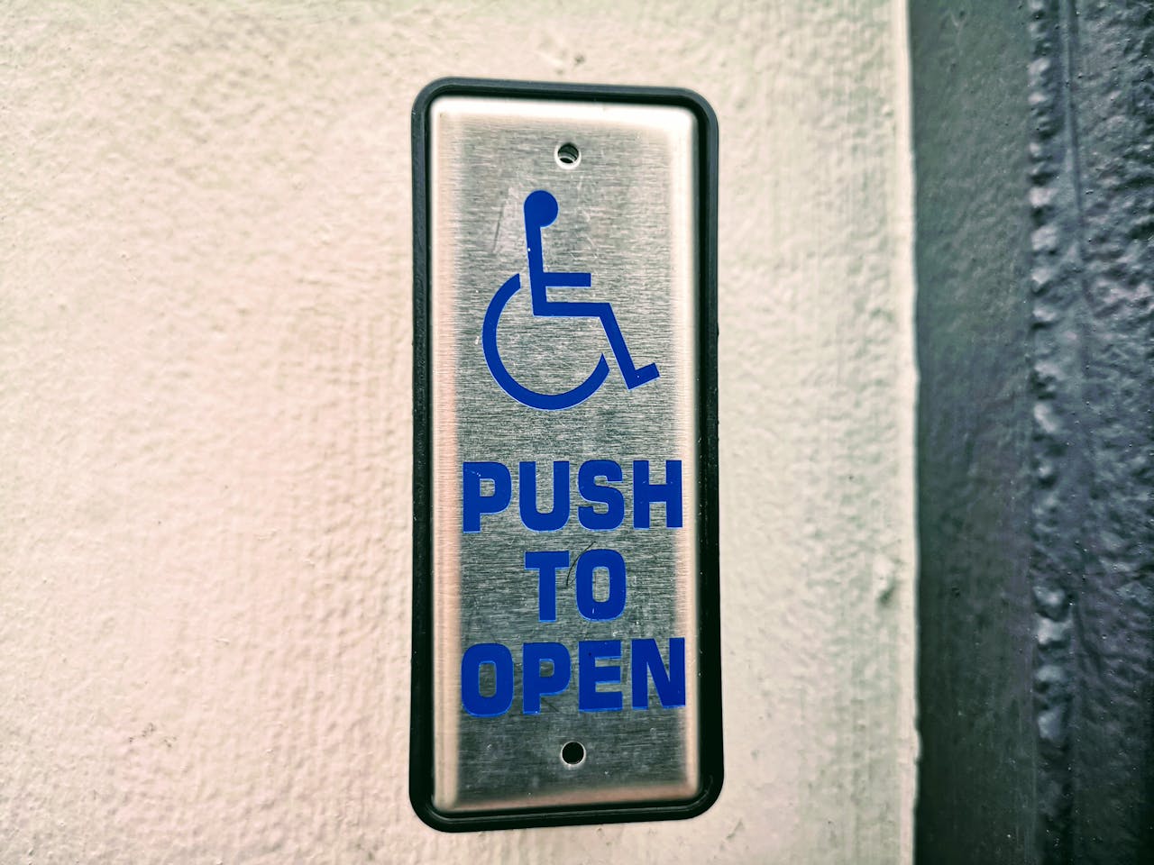 Close-up of a push button sign for accessibility on a white wall.