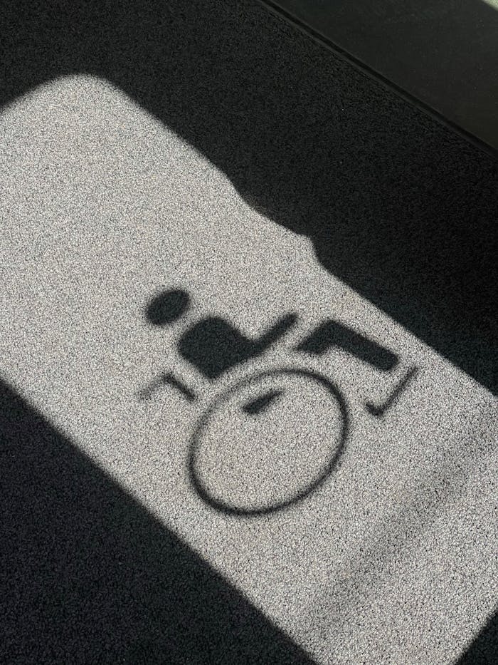 Shadow of a wheelchair symbol projected on a textured floor, indicating accessibility.